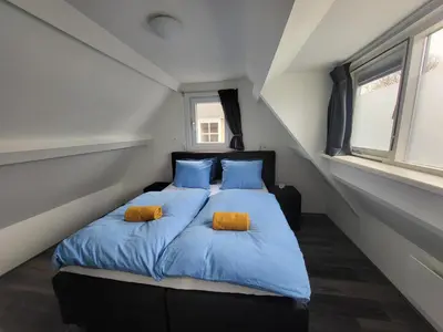 a bedroom with a bed with blue sheets and two orange pillows at FlipFlop in Noordwijk aan Zee
