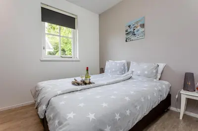 a bed with a white comforter with a bottle and glasses on it at De Gouden Spar in Noordwijk
