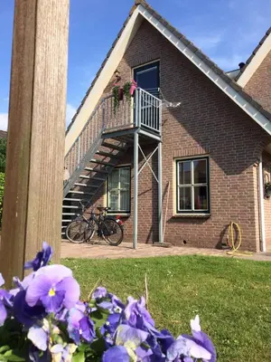 a house with a staircase and purple flowers in the yard at De Slotruine in Egmond aan den Hoef