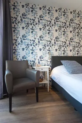 a bedroom with a bed and a chair and a wall at Hotel Faber in Zandvoort