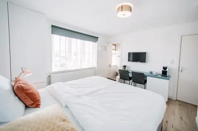 a white bedroom with a large bed and a desk at Zylt Zandvoort in Zandvoort