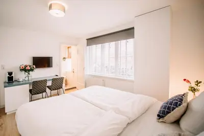 a white bedroom with a bed and a table at Zylt Zandvoort in Zandvoort