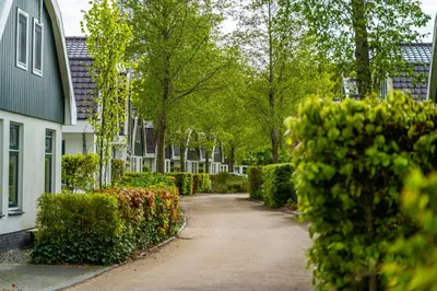 a walkway through a garden with bushes and houses at Europarcs Koningshof in Schoorl