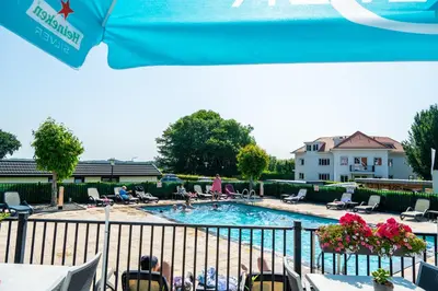a swimming pool with people sitting in chairs around it at EuroParcs Noordwijkse Duinen in Noordwijk aan Zee
