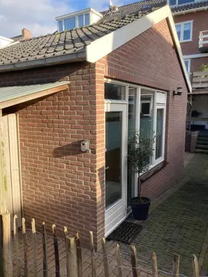 a brick house with a white door and a fence at Lodge in Noordwijk