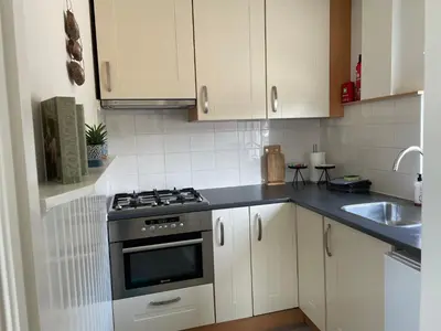 a kitchen with white cabinets and a stove and a sink at Me Oissie in Egmond aan Zee