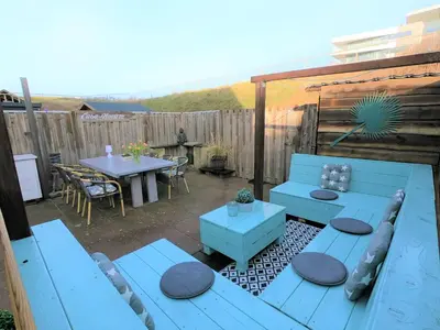a patio with blue benches and a table and a fence at Casa Nuestra in Egmond aan Zee