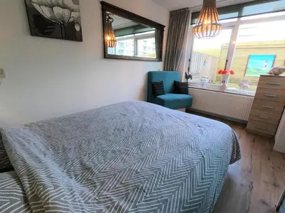 a bedroom with a bed and a chair and a window at Casa Nuestra in Egmond aan Zee