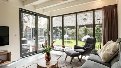 a living room with large windows and a couch and chairs at Dutchen Vakantiepark Duynvoet in Schoorl