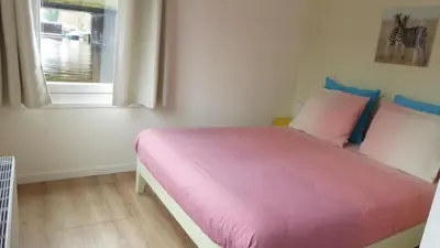 a bedroom with a pink bed with a window at Houseboat In The Center, 5 min walk to Tropical Museum, Free Wifi! in Amsterdam