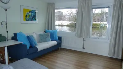 a living room with a blue couch and a window at Houseboat In The Center, 5 min walk to Tropical Museum, Free Wifi! in Amsterdam