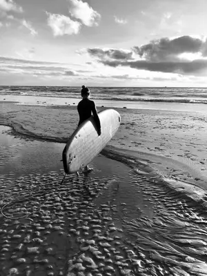 a man is holding a surfboard on the beach at Hotel Neptunus in Egmond aan Zee