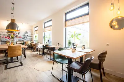 a restaurant with tables and chairs and a large window at Hotel Neptunus in Egmond aan Zee