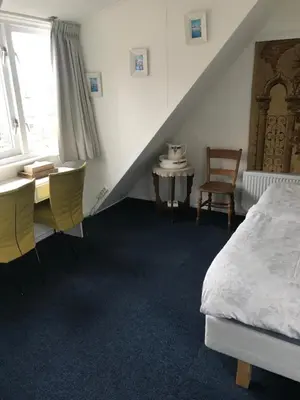 a bedroom with a bed and a desk and a window at B&B De Duinhoek in Beverwijk
