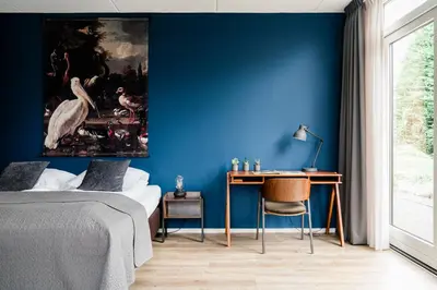 a bedroom with a blue wall with a desk and a bird painting at de Logerie in Enkhuizen