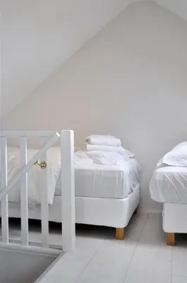 a white bedroom with a bed and a staircase at Beachhouse Bosweg in Noordwijk aan Zee