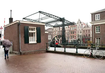 a person with an umbrella walking down a street with a building at SWEETS - Scharrebiersluis in Amsterdam