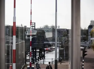 a man walking down a street next to a river at SWEETS - Westerdoksbrug in Amsterdam