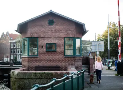 a woman walking a dog in front of a brick building at SWEETS - Kattenslootbrug in Amsterdam