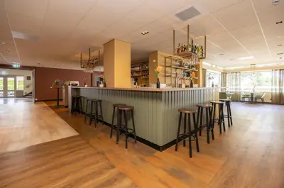 a bar with stools in a large room at Fletcher Hotel-Restaurant Het Witte Huis in Amersfoort