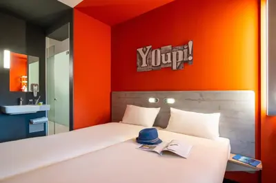 a bedroom with a white bed with an orange wall at ibis budget Amsterdam Airport in Badhoevedorp