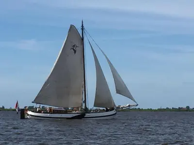 a sailboat with white sails on a body of water at Tjalkjacht Pelikaan Volendam in Volendam