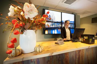 a woman standing at a desk with a vase of flowers at Best Western Zaan Inn, Amsterdam - Zaandam in Zaandam