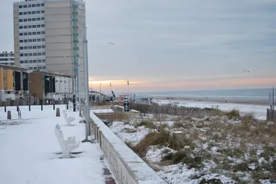 a snow covered beach with a white bench and a building at Appartement in Zandvoort in Zandvoort