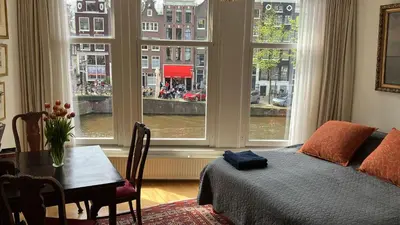 a bedroom with a bed and a table and windows at Canal View B&B Amsterdam in Amsterdam