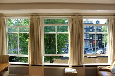 a living room with three windows with curtains at Amsterdam Jewel Canal Apartments in Amsterdam
