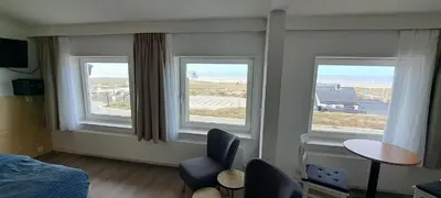 a bedroom with three windows and a chair and a table at Bed&Breakfast aan Strand in Katwijk aan Zee