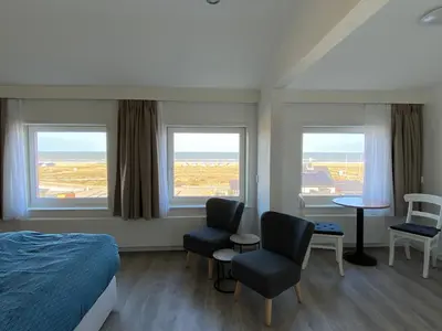 a bedroom with two chairs and a bed and two windows at Bed&Breakfast aan Strand in Katwijk aan Zee