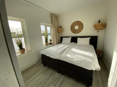 a bedroom with a bed and two windows at Eb en Vloed Katwijk in Katwijk
