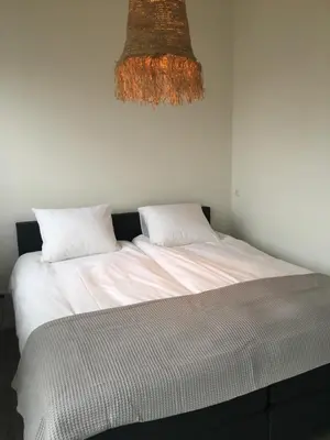 a bedroom with a bed with white sheets and a chandelier at Eb en Vloed Katwijk in Katwijk