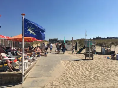 a beach with a flag and people walking down a sidewalk at Eb en Vloed Katwijk in Katwijk