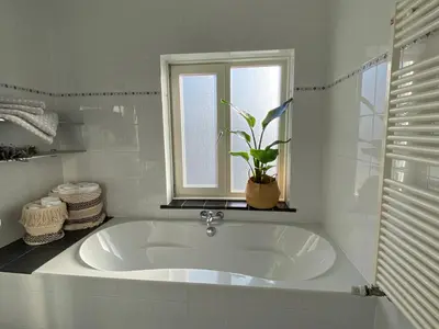 a white tub in a bathroom with a potted plant at Eb en Vloed Katwijk in Katwijk