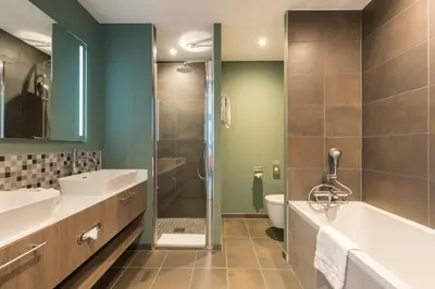 a bathroom with a tub and a sink and a shower at Leonardo Royal Hotel Amsterdam in Amsterdam