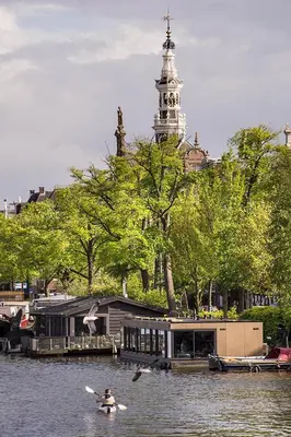 a person kayaking on a river with a clock tower at Houseboat Amsterdam - Room with a view in Amsterdam