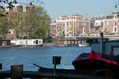 a boat docked at a dock on a river with buildings at Houseboat Little Amstel in Amsterdam