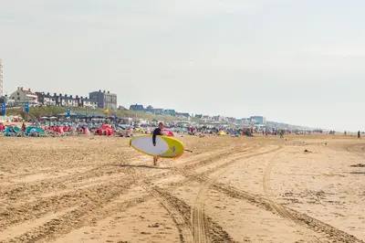 a man walking on the beach with a surfboard at Holiday Beach House in Zandvoort