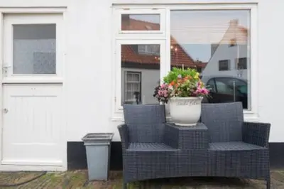 a wicker chair and a vase with flowers on a porch at 't Zandhuisje in Zandvoort