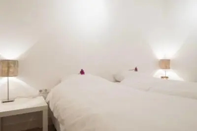a white bedroom with a white bed and two lamps at 't Zandhuisje in Zandvoort