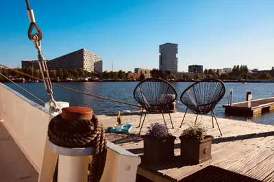 a boat with two chairs on a dock next to the water at Sailor Suite Coaster Mado in Amsterdam