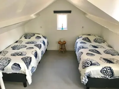 a attic bedroom with two beds and a window at Ferienhaus Glücklich am Meer 3 mit Wellnesszugang in Egmond aan Zee