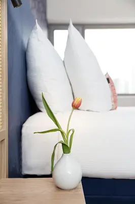 a flower in a vase on a table next to a bed at Boutique Apartments Amsterdam in Amsterdam