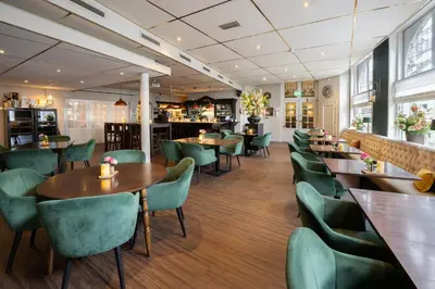 a restaurant with wooden tables and green chairs at Hotel Royal in Noordwijk