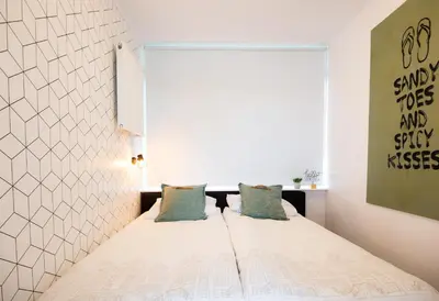 a bedroom with a bed with white sheets and blue pillows at Appartement Zuyd in Zandvoort