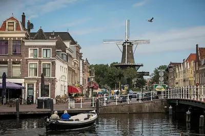 two people in a boat in a canal with a windmill at City Hotel Rembrandt in Leiden