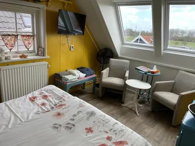 a bedroom with a bed and two chairs and a tv at Bed and Breakfast De Pepersteeg in Marken