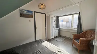 a bedroom with a bed and a chair and a window at Beach-house27 in Egmond aan Zee
